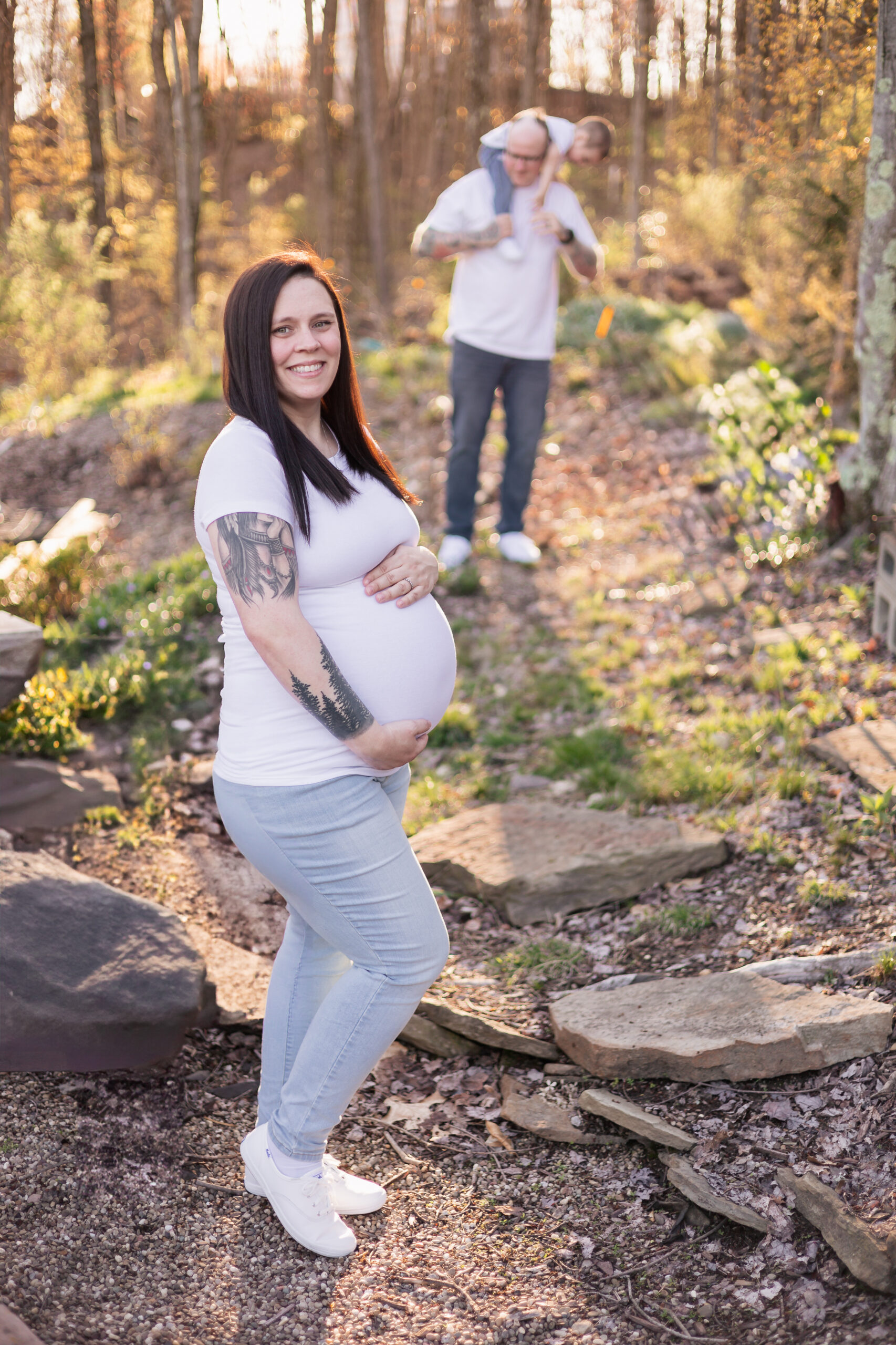 Mara showing off her pregnant belly with Michael playing with Tanner in the background. 